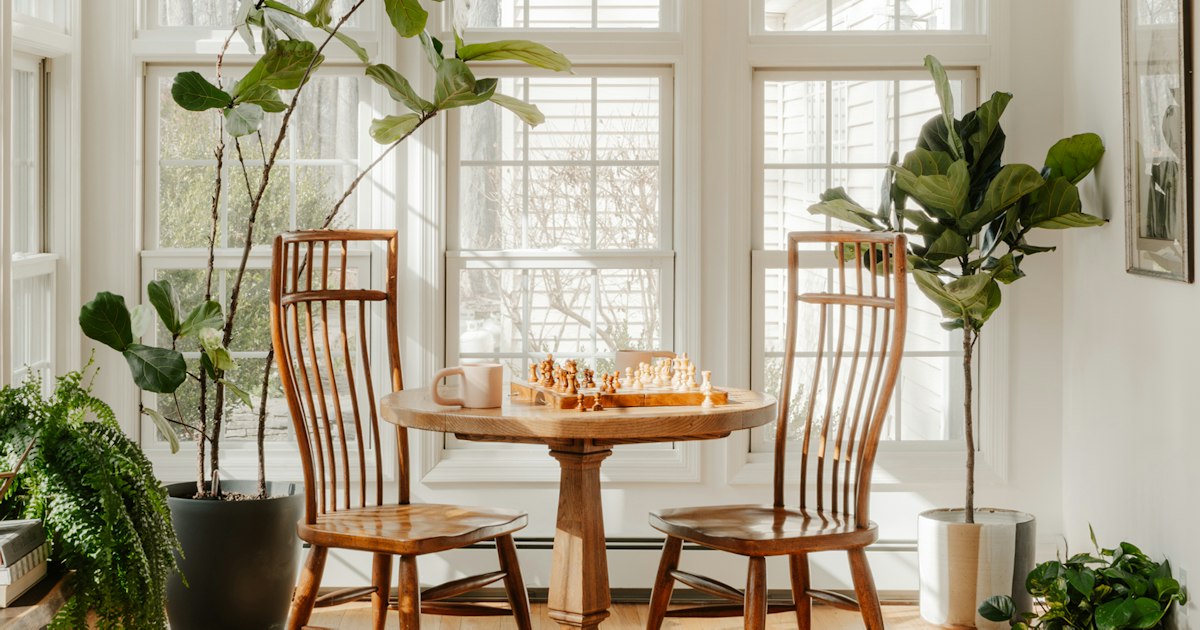 2 empty wooden chairs at a small table with a chess game in progress, in a sunlit room