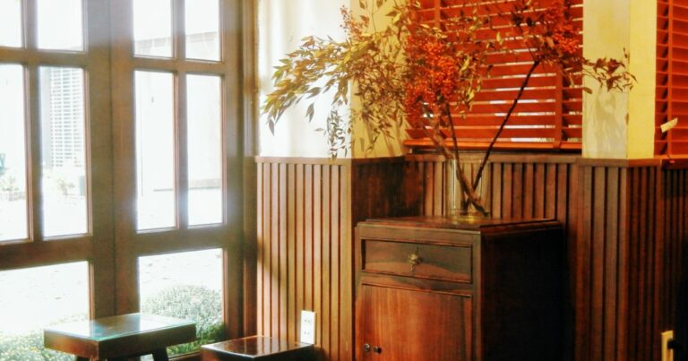 Branches with orange berries in a glass vase on a wooden cabinet, lit by afternoon sun from a tall window