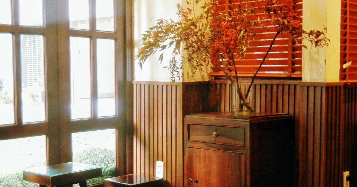 Branches with orange berries in a glass vase on a wooden cabinet, lit by afternoon sun from a tall window
