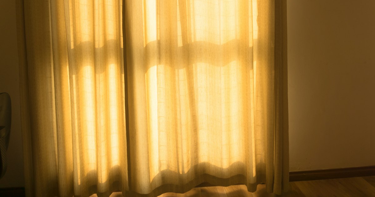 Morning sunlight glowing through pale linen curtains onto a wooden floor