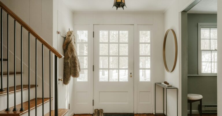 A bright entrance hall with a white glazed front door, a coat on a hook, boots on the mat and a wooden staircase