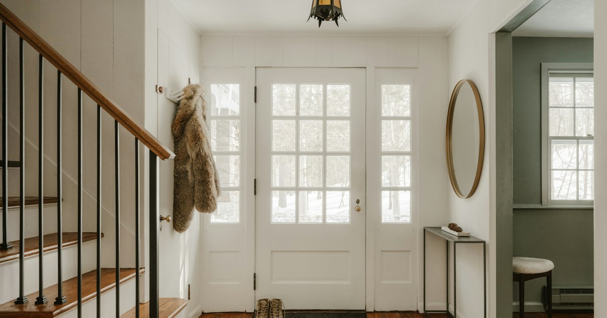 A bright entrance hall with a white glazed front door, a coat on a hook, boots on the mat and a wooden staircase