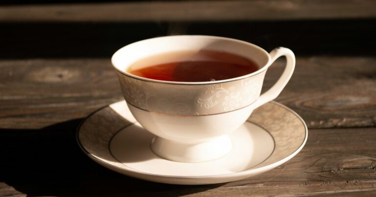A cup of tea on a saucer resting on a weathered wooden table in warm sunlight