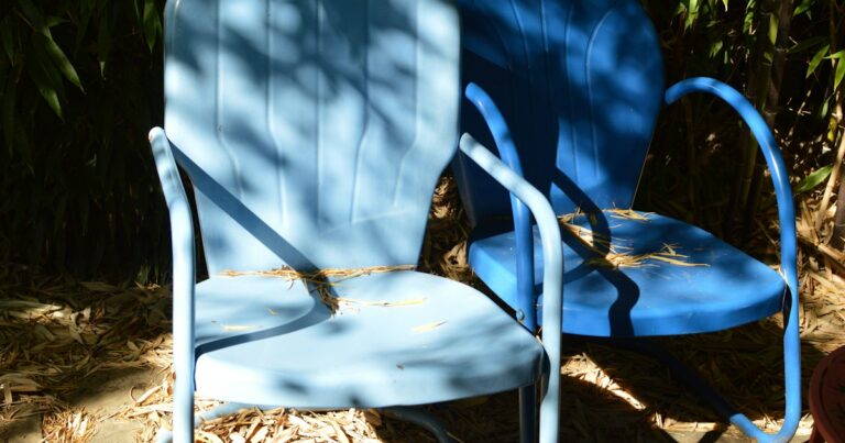 2 blue metal garden chairs side by side in dappled sunlight, angled slightly apart