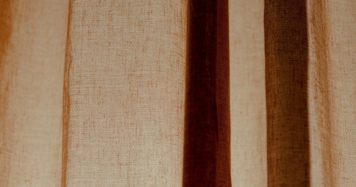 Folds of a warm brown linen curtain lit from behind