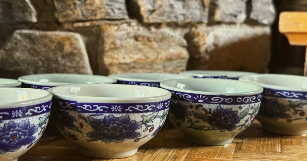 A row of hand-painted blue and white ceramic bowls on a woven mat against a warm stone wall