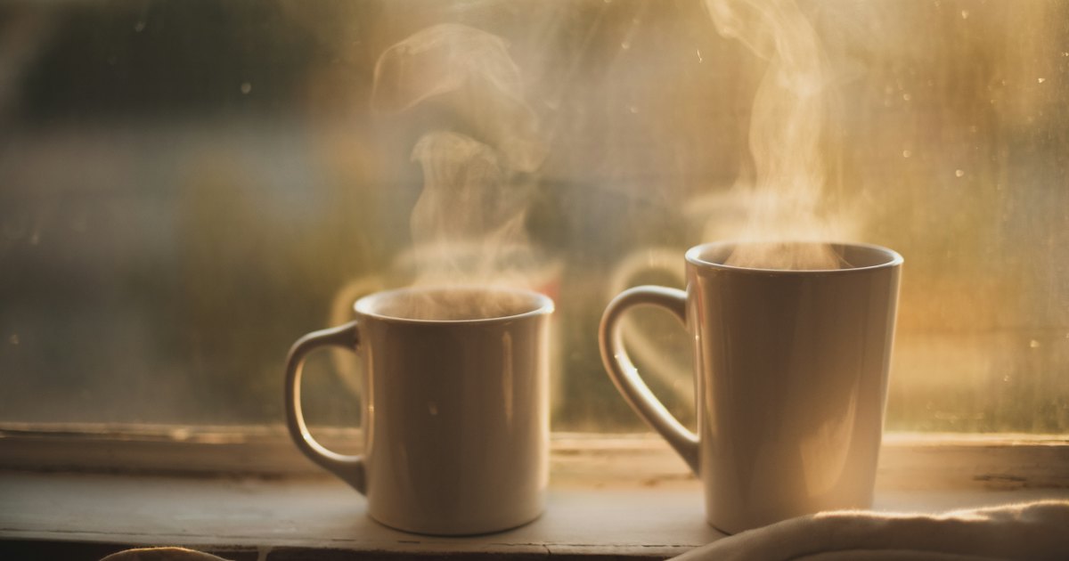 2 steaming mugs on a windowsill in warm early light, with a soft blanket beside them