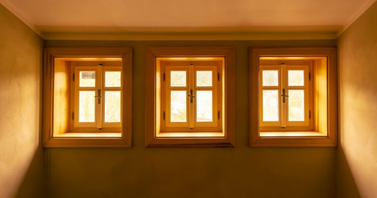 Three small wooden-framed windows in a quiet room, glowing with warm daylight