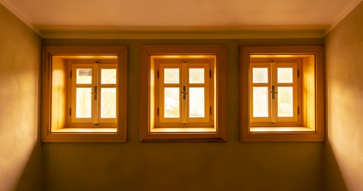 Three small wooden-framed windows in a quiet room, glowing with warm daylight