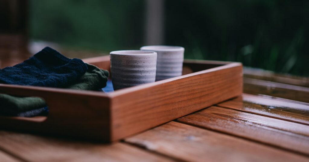 Two speckled ceramic cups side by side in a wooden tray on an outdoor wooden table