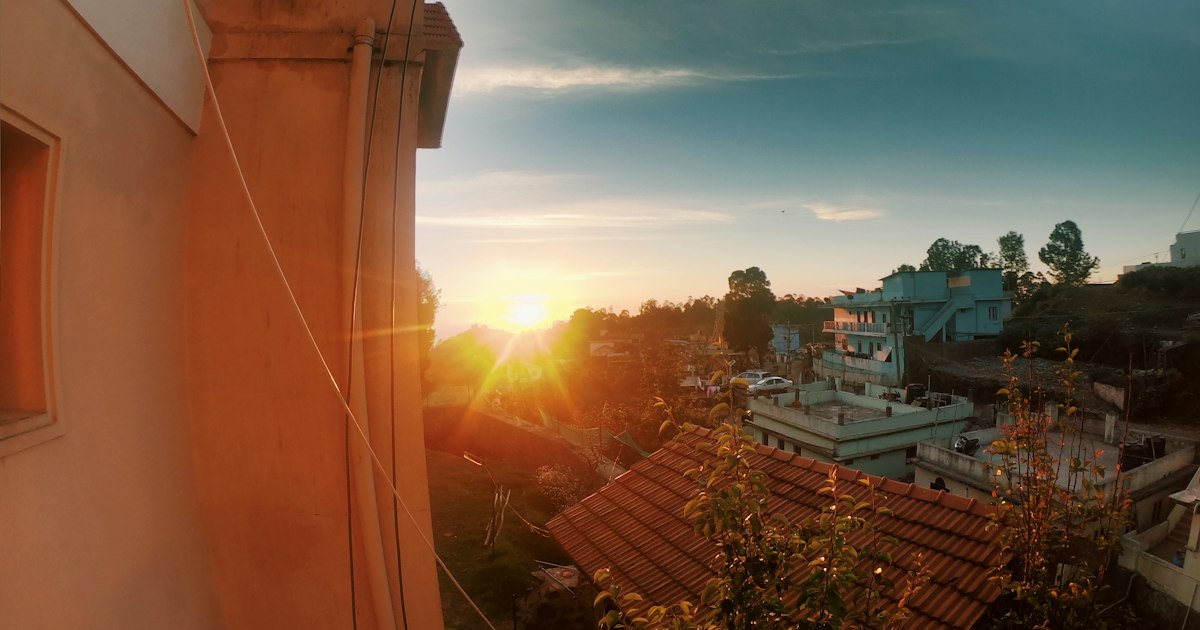 Low sun setting over the tiled rooftops of a hillside town, seen from beside a warm-coloured wall