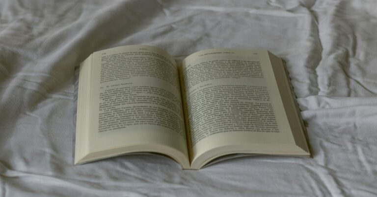 An open paperback book lying on soft white bed linen