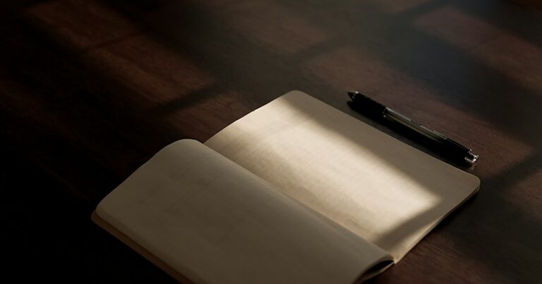 An open blank notebook and a pen on a wooden table in a band of warm sunlight