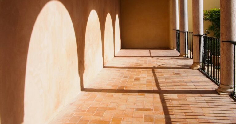 Sunlight casting a row of identical arch shapes along a warm terracotta gallery