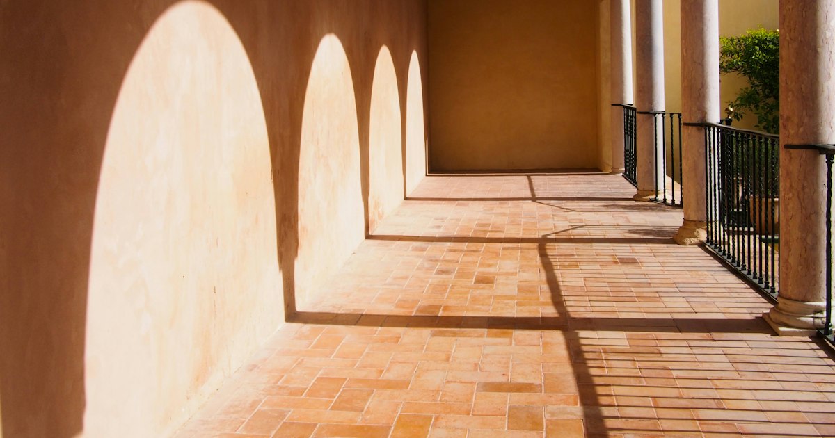 Sunlight casting a row of identical arch shapes along a warm terracotta gallery