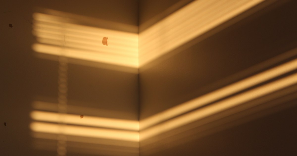 Warm bands of evening sunlight falling through blinds onto the corner of a plain room