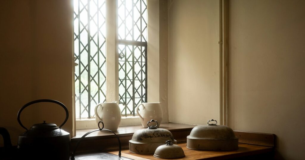 White jugs, a kettle and covered serving dishes by a sunlit leaded window