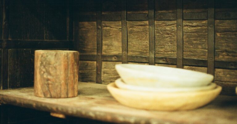 Stacked pale bowls and a wooden pot on an old wooden shelf in warm light