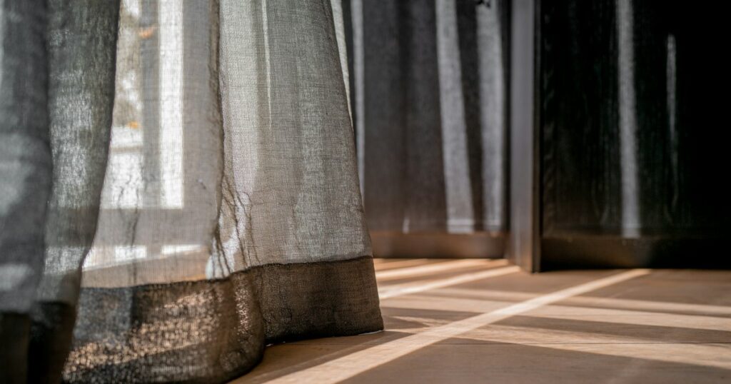 Warm sunlight falling across a wooden floor through a sheer linen curtain