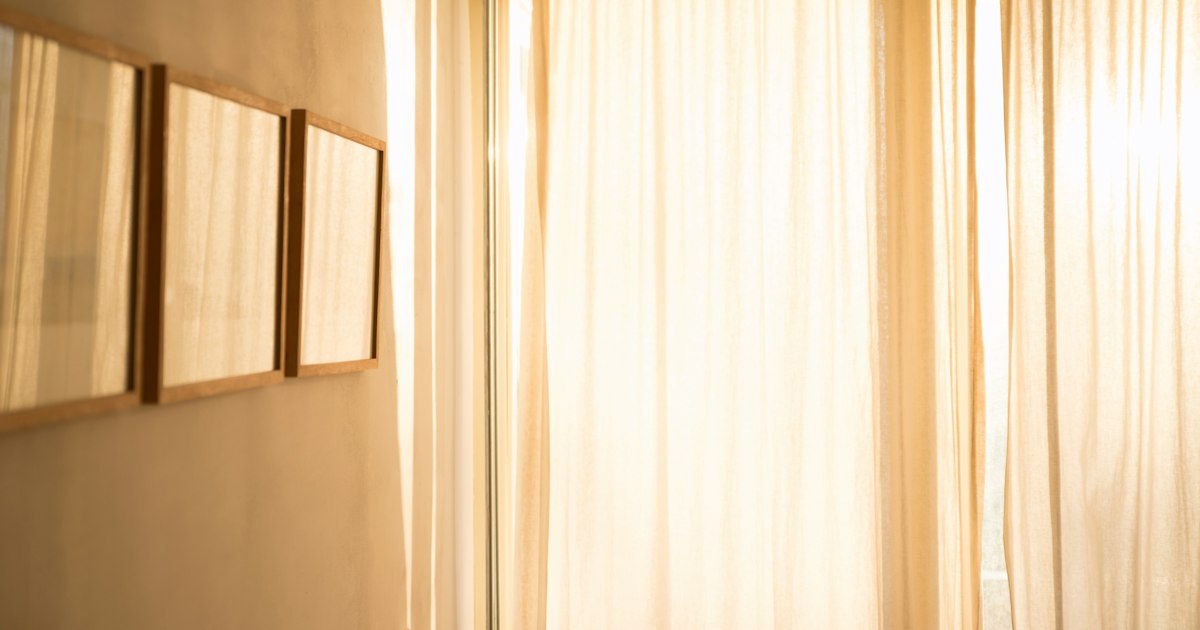 Bright sunlight through pale linen curtains beside 3 empty wooden picture frames on a cream wall