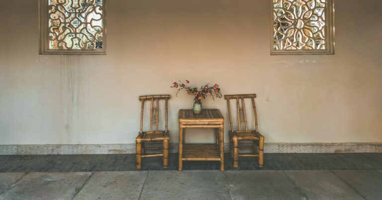 Two bamboo chairs and a small table with a posy against a pale wall