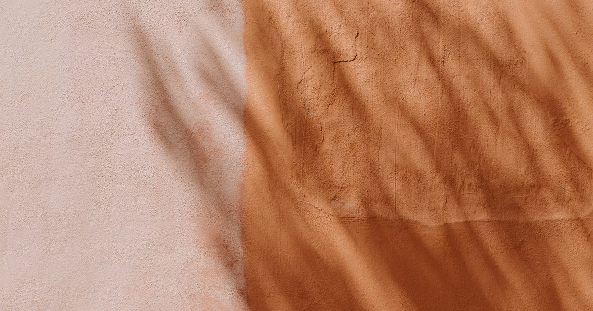 A plaster wall painted half pale pink and half terracotta, with soft leaf shadows falling across both colours