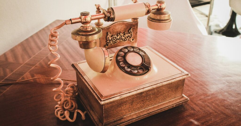 An old cream rotary telephone with a coiled cord on a polished wooden table in warm light