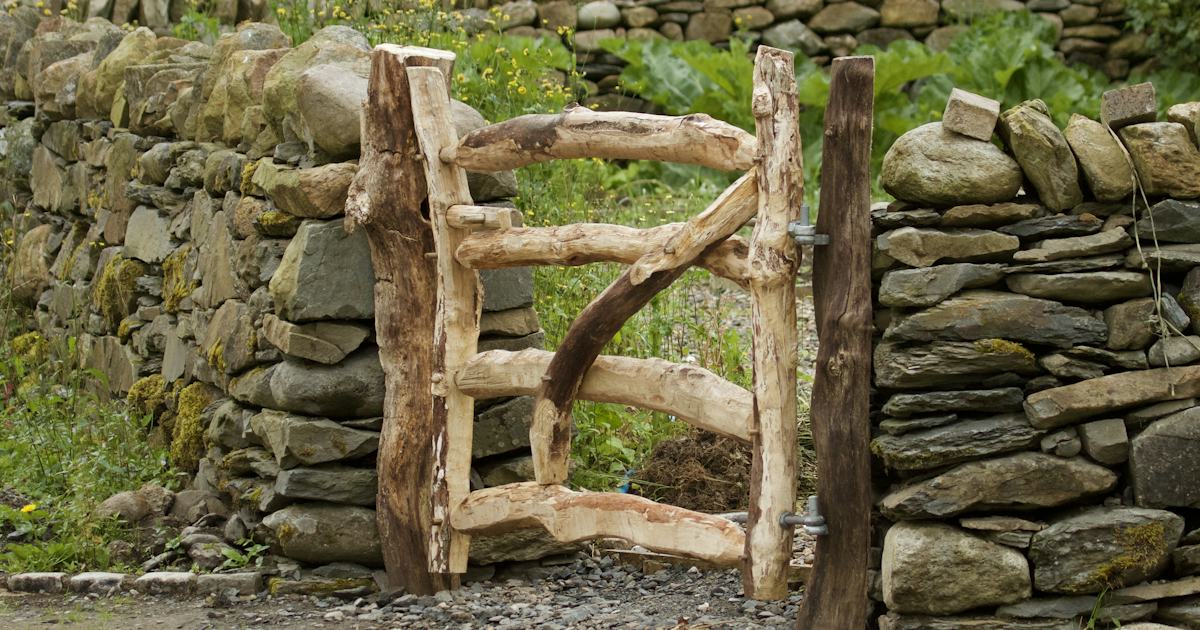 A rustic wooden gate set in a dry stone wall, with a green garden visible beyond it