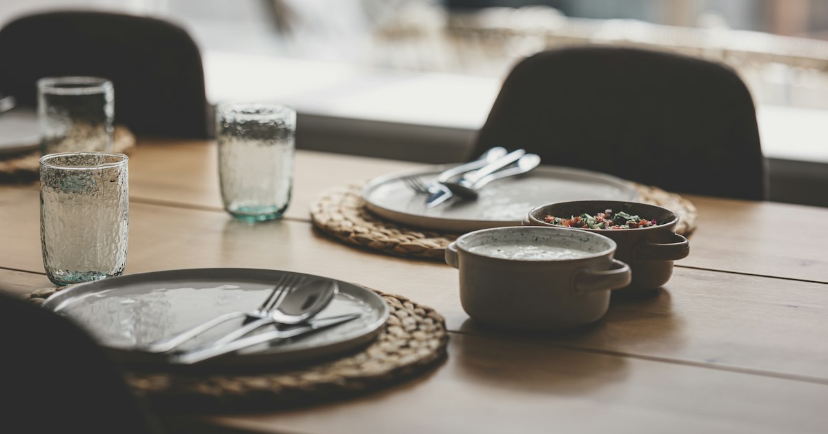 A wooden dining table laid for 2, with plates, cutlery, glasses and 2 small bowls set opposite each other